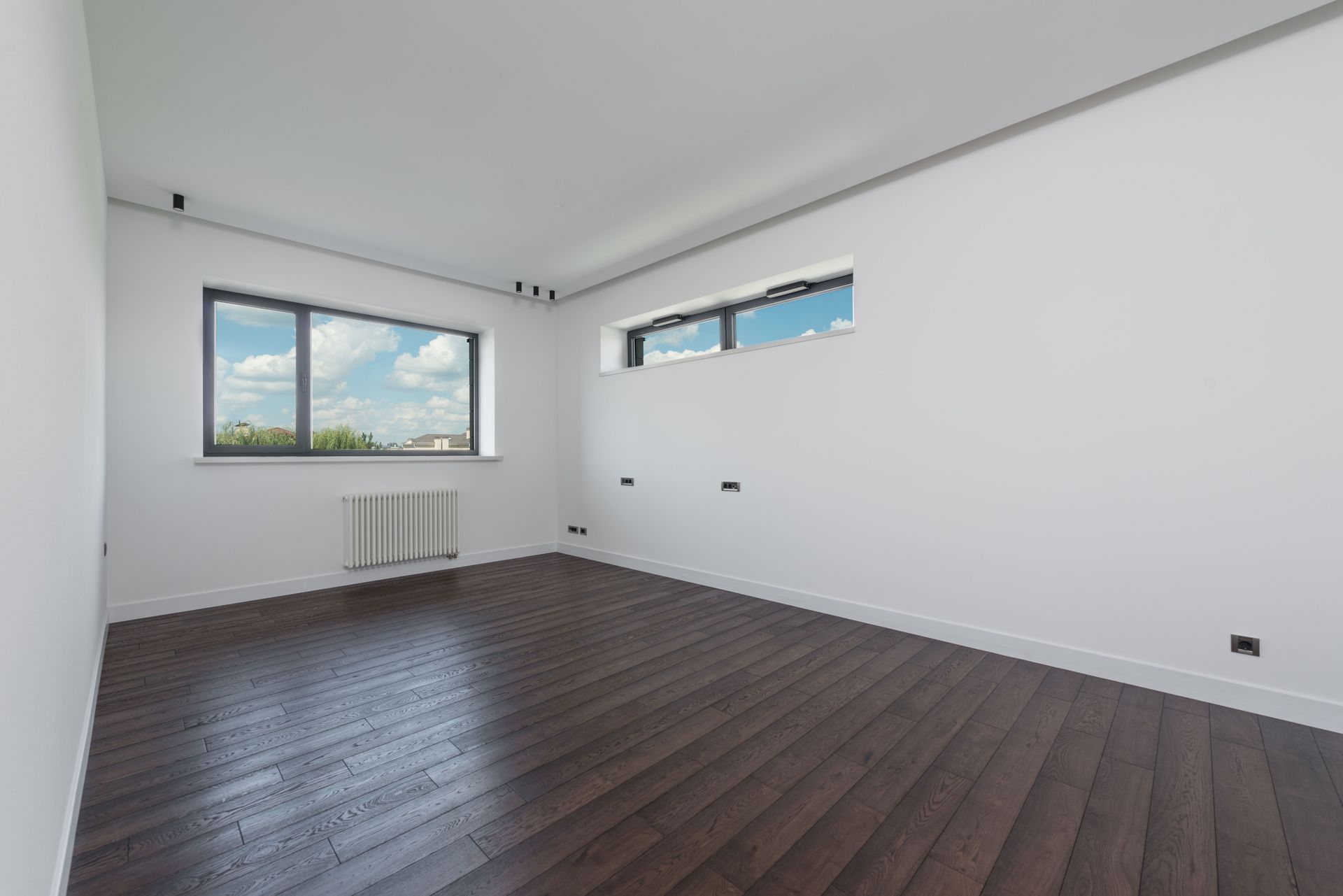 Interior of empty spacious room with laminated floor big windows white walls and ceiling in daylight
